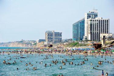 אנשים מבלים בחוף הים וברקע המלונות